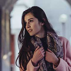 Woman in pink coat and scarf standing in archway.