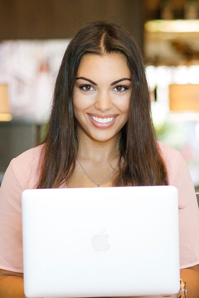 A woman smiling and holding a laptop.