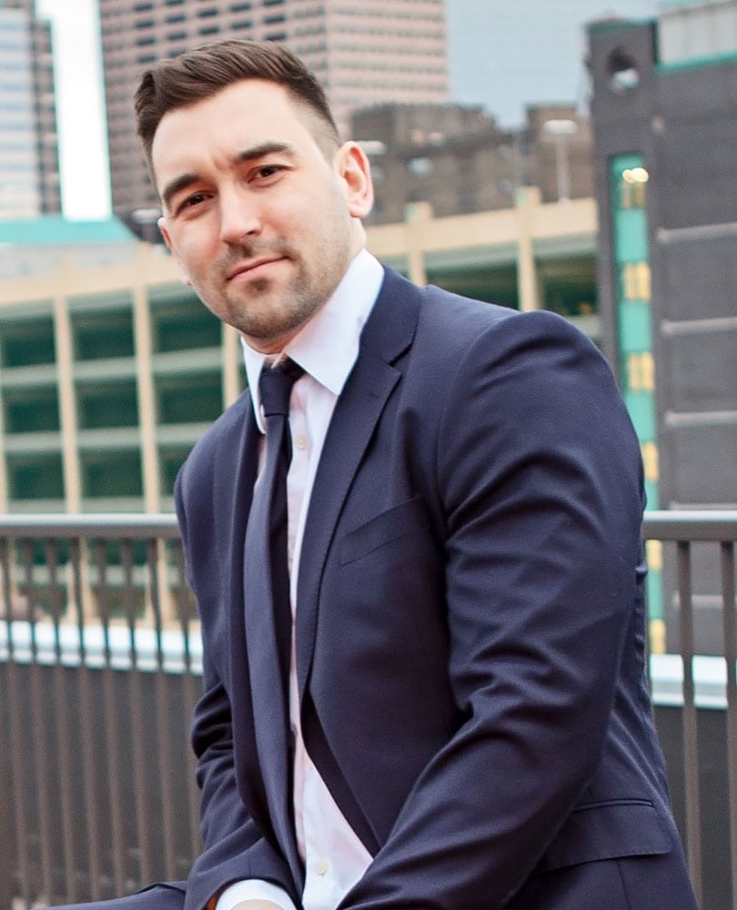 A man in a suit and tie sitting on a ledge overlooking a city skyline.