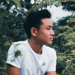 A young man sitting on a bench in the woods.