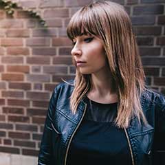 Woman in black leather jacket standing in front of brick wall.